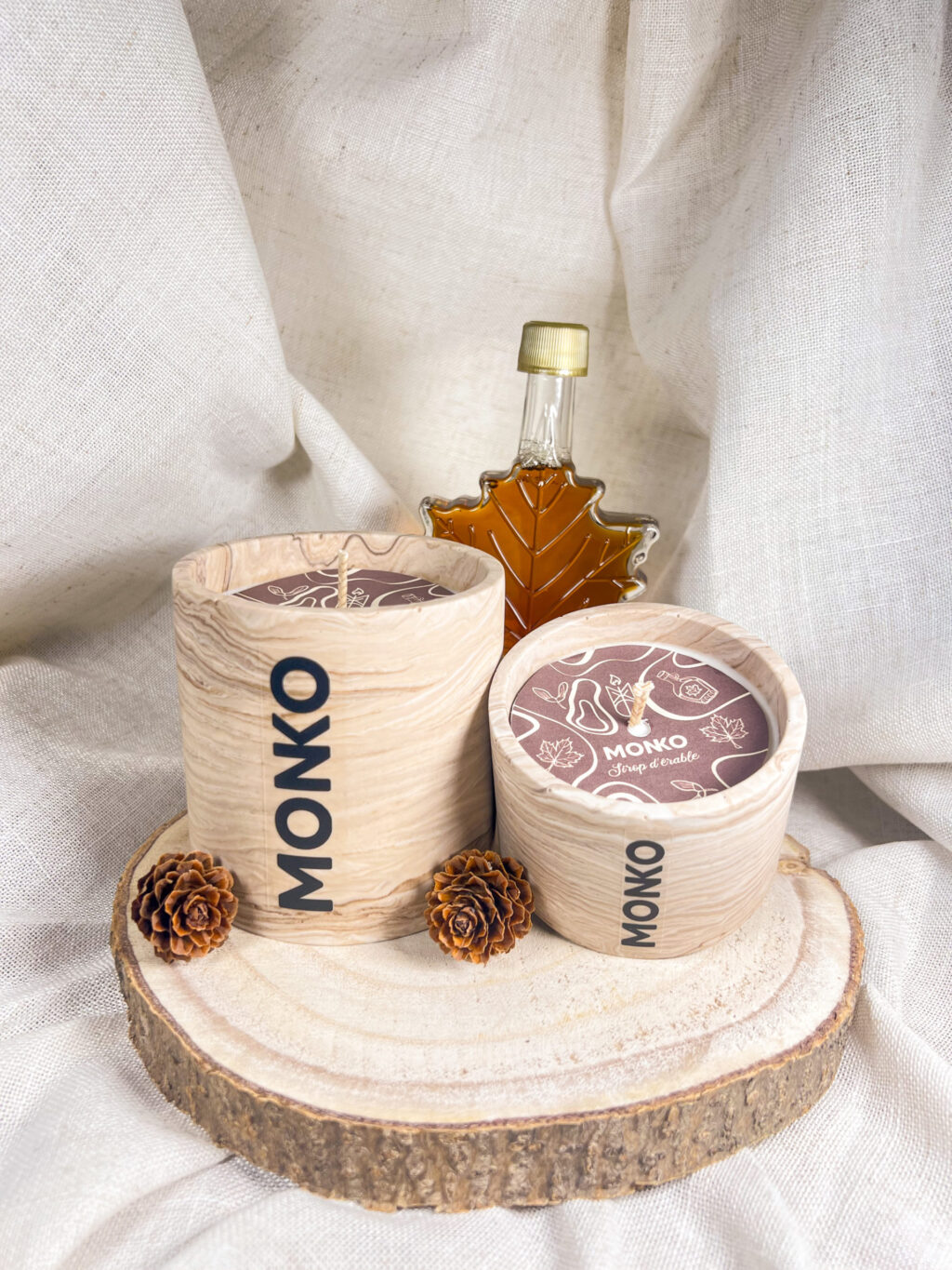 Bougie 120g et 300g sur un rondins de bois avec en fond du sirop d'érable dans une fiole en forme de feuille d'érable.